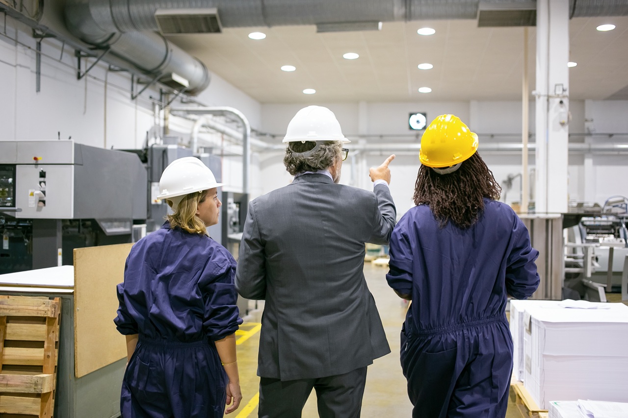 Engenheiro industrial liderando equipe técnica em inspeção completa pelo chão de fábrica para diagnóstico de processos e identificação de oportunidades de evolução.