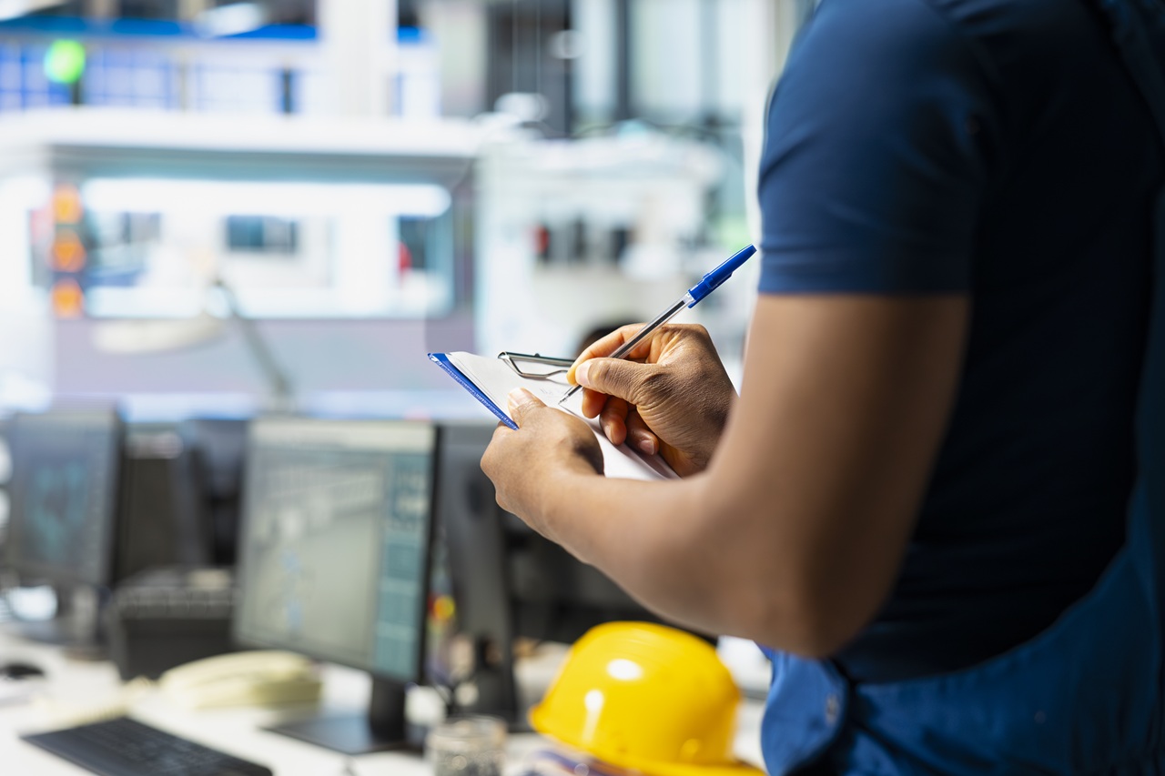 Engenheiro ou técnico industrial realizando inspeção de qualidade e registro de dados operacionais em planta fabril.